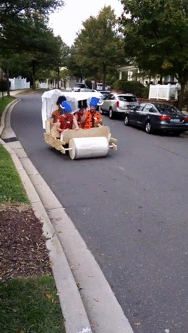 four men dressed in flinstones costumes riding in a DIY foot powered caveman vehicle